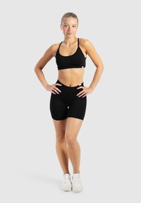 Zwart sportbeha en hoogwaisted shorts set gemaakt van rekbare stof. Heeft een eenvoudig ontwerp met verstelbare banden. Witte sneakers maken de look compleet.