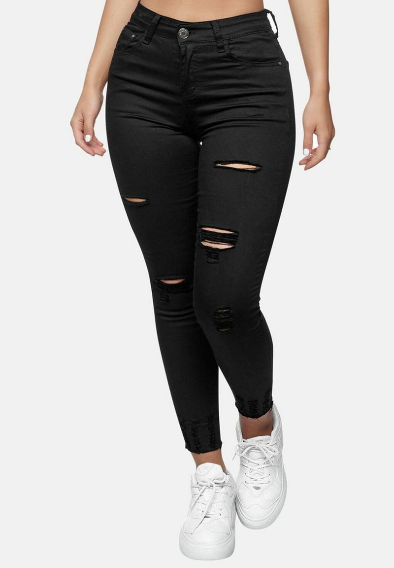 Black denim skinny jeans with ripped detailing, high-waisted design, and fitted silhouette. Paired with white sneakers.
