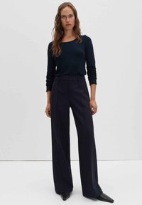 Haut bleu marine à manches longues avec un décolleté carré, associé à un pantalon noir taille haute à jambes larges. Texture lisse et coupe sur mesure.