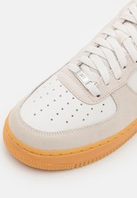 Vita och beige mockaskor med perforerat tåparti, texturerad överdel och orange gummisula. Har platta snörning och metallisk logodetalj.