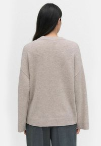 Beżowy, oversize sweter wykonany z miękkiej dzianiny, z okrągłym dekoltem, opuszczonymi ramionami i ribbowym wykończeniem u dołu.