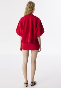 Rode oversized sweatshirt met brede mouwen, gecombineerd met een strakke rode minirok. Glad oppervlak; minimale details en accenten.