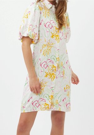 Weißes knielanges Kleid mit gelben, pinken und grünen Blumenmustern, gepufften kurzen Ärmeln und einem Kragen, getragen von einer stehenden Person.