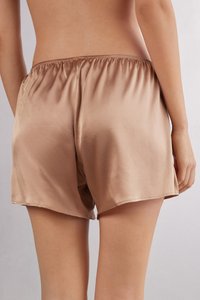 Pantalones cortos de satén beige con cinturilla elástica, que presentan un ajuste holgado y una textura suave, mostrados desde atrás sobre un fondo neutral.