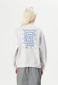 Felpa grigia chiara con maniche lunghe, caratterizzata da una grafica blu e il testo "FIND YOUR SOUL" sulla parte posteriore.