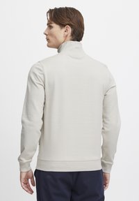 Beige mock-neck sweatshirt with long sleeves and ribbed cuffs, featuring a smooth texture and elastic hem for a fitted look.