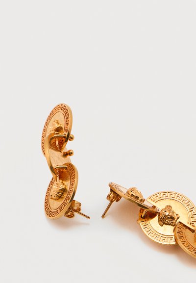 Χρυσά σκουλαρίκια καρφωτά με συνδεδεμένους κυκλικούς δίσκους που φέρουν μοτίβα ελληνικού κλειδιού και ανάγλυφες κεφαλές λιονταριού σε λευκό φόντο.