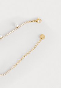 Bracciale dorato con rhinestones trasparenti e perle bianche, dotato di chiusura a gancio e di una breve catena di estensione per la lunghezza regolabile.