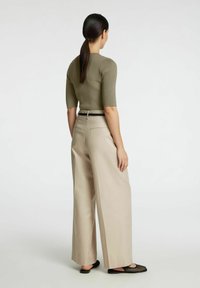 Olivno zelena rebrasta majica s rukavima do lakta, u kombinaciji s svijetlosmešim hlačama širokog kroja. Crni remen i crne sandale s otvorenom pertom.