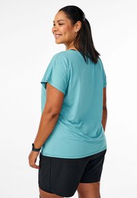 Turkoosi urheilu paita, jossa on lyhyet hihat, valmistettu sileästä ja kevyestä kankaasta. Yhdistetty mustiin shortseihin, joissa on rento istuvuus.