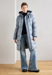 Lichtblauwe gewatteerde jas met capuchon, voorzien van een gevoerde binnenkant, ritssluiting en een oversized pasvorm, gecombineerd met brede denim jeans.