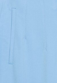 Jasnoniebieska, teksturowana tkanina z ukośnym splotem, z boczną kieszenią i subtelnym detalem w postaci przeszycia. Skrojony, prosty krój nogawki.