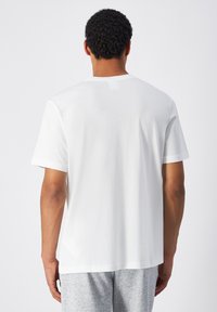 Camiseta de algodón blanca con cuello redondo y mangas cortas, que presenta un corte relajado y una textura suave. La vista trasera no muestra ninguna marca visible.