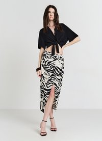 Chemise noire courte boutonnée avec un nœud à l'avant, associée à une jupe beige à motif zèbre noir avec une fente haute sur la cuisse. Lanières noires à la cheville.