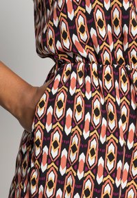 Vestido de patrón multicolor con formas geométricas en naranja, rosa, blanco y negro. Incluye un bolsillo lateral y una cinturilla elástica.