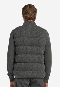 Grau gestrickte Weste mit Zopfmuster, ausgestattet mit einem hohen Kragen und gesteppeten Steppabschnitten im Pufferstil zur Isolierung. Strukturierter Stoff mit gerippten Bündchen.