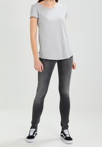 Šedé tričko s krátkým rukávem a kulatým výstřihem, v kombinaci s tmavě šedými skinny džíny a černými teniskami s bílými akcenty.