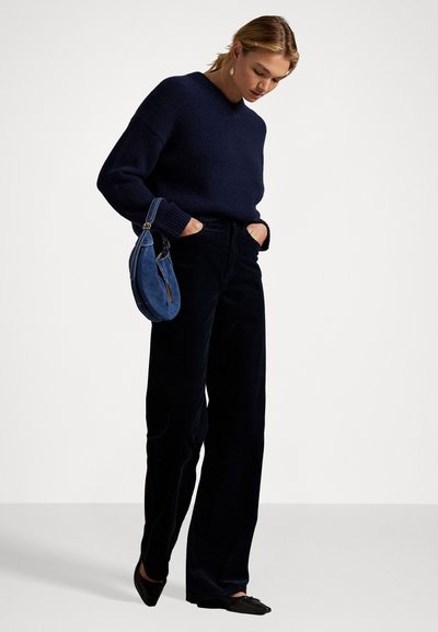 Navy knitted sweater with a v-neck, paired with black wide-leg pants. A small blue suede bag with a short handle is held in the left hand.