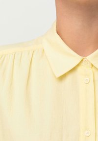 Żółta koszula z guzikami, z klasycznym kołnierzykiem, miękką teksturą i detalami pintuck wzdłuż ramion.