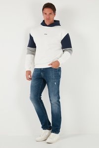 Hvid hættetrøje med navy, grå og hvid farveblokering; lange ærmer; front kangaroo-lomme; parret med lyseblå slidte jeans og hvide sneakers.