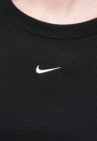 Čierna rebrovaná látka na mikine s okrúhlym výstrihom a malým bielym logom Nike na hrudi. Textúrovaný povrch s horizontálnymi líniami.