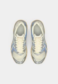 Ténis de corrida leves com parte superior em malha nas cores bege e azul, sola texturada e atacadores creme. Logótipo Asics na língua.