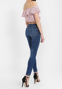 Modré skinny džíny s přiléhavým střihem, vysokým pasem a hladkou texturou. V kombinaci s pruhovaným topem bez ramínek a černými podpatky.