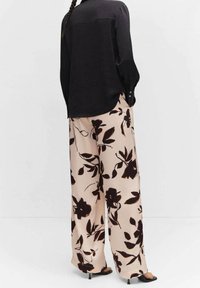 Chemise noire à boutons avec une texture lisse, associée à un pantalon beige large avec un grand motif floral sombre. Design long et ample.