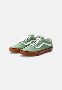 Green suede sneakers with white accents and laces, featuring a low-profile design and brown rubber soles.
