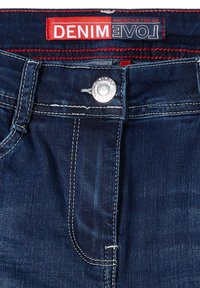 Granatowe dżinsy z ciemnego denimu z srebrnym zapięciem na zatrzask, widocznymi szwami oraz czerwoną metką z napisem "DENIM LOVE" na pasku.