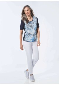 Korte mouwen blauw-wit gemarmerde top met effen marineblauwe zijkanten, gecombineerd met witte slim-fit broek en lichtgrijze sneakers.