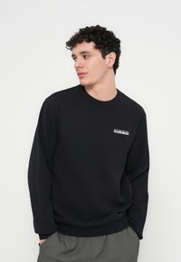 Felpa nera con maniche lunghe e polsini a costine. Presenta un piccolo logo bianco sul petto. Tessuto liscio con una vestibilità comoda.