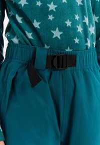 Tyrkysové kalhoty s opaskem s černou sponou, vyrobené z hladkého, lehkého materiálu. Spárováno s tyrkysovým fleecovým topem s hvězdným vzorem.