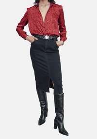 Rode blouse met bloemenpatroon, zwarte denim pencil skirt met een vooropening, en kniehoge zwarte gebreide laarzen met hoge hakken. Riem met ronde gesp.