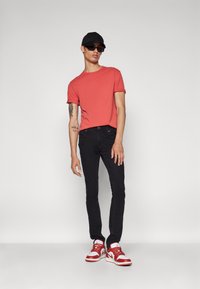 Camiseta corta roja, jeans skinny negros y zapatillas rojas y blancas. Una gorra negra y gafas de sol añaden contraste. Textura de tela suave.