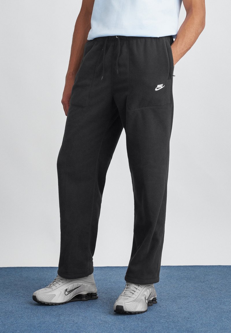 Fekete mikroszálas melegítőnadrág elasztikus derékkal, két elülső zsebbel és fehér Nike logóval a bal combon. Az anyag puha és texturált.