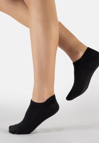 Calcetines negros de corte bajo fabricados con un tejido elástico, que presentan un diseño sin costuras y un puño acanalado, parcialmente visibles en un pie en movimiento.