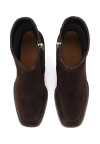 Botas de tobillo de ante marrón con una textura suave, punta cuadrada y detalles de cremallera plateados. El interior está forrado en negro.