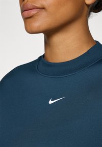 Sweatshirt Nike bleu foncé avec col à côtes, présentant un petit logo blanc sur la poitrine, texture lisse et design ajusté.