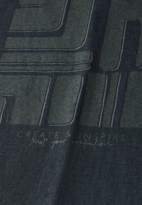 Tela de color verde oscuro con un diseño gráfico que presenta líneas y texto gris claro "CREA E INSPIRA" en un acabado suave y texturizado.