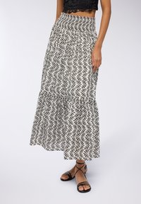 Gonna maxi bianca con stampa di foglie nere, dotata di vita arricciata e fondo a strati. Abbinata a sandali neri con lacci.