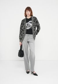 Grå, fluffy cardigan med sorte leopardpletter, båret over en sort grafisk t-shirt, parret med lysegrå jeans og en sort taske. Sorte højhælede sko.
