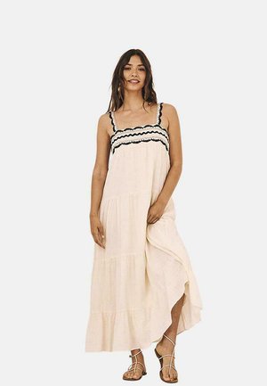 Vestido maxi de tela beige claro, con un diseño en capas, ribete negro con forma de onda en el corpiño y tirantes ajustables.