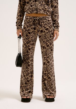 Brown patterned wide-leg pants with floral and animal prints, featuring a drawstring waist. Paired with a black handbag and platform shoes.