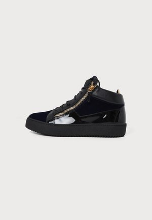 Μαύρο sneaker ψηλός με γυαλιστερά δερμάτινα πάνελ, πλευρικό φερμουάρ, κορδόνια και χοντρή μαύρη ελαστική σόλα σε ανοιχτό φόντο.