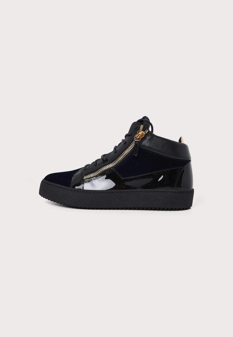 Μαύρο sneaker ψηλός με γυαλιστερά δερμάτινα πάνελ, πλευρικό φερμουάρ, κορδόνια και χοντρή μαύρη ελαστική σόλα σε ανοιχτό φόντο.