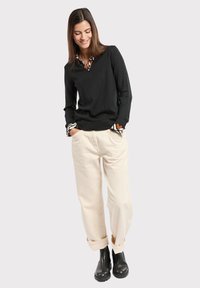 Pull noir à col en V, manches longues avec des poignets à motifs, associé à un pantalon crème et des bottines noires. Texture lisse, coupe décontractée.