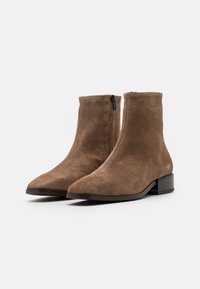 Bottines en suédine brune avec fermeture éclair, bout pointu et petit talon carré, présentant des coutures visibles et une texture lisse.