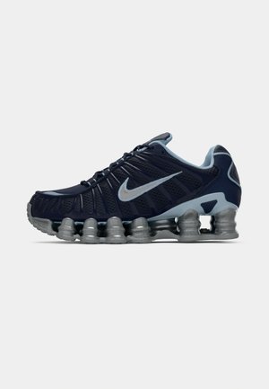 Dunkelblaue und silberne Sportschuhe mit segmentierter, gepolsterter Sohle und silbernem Nike-Swoosh an der Seite, im rechten Profil vor weißem Hintergrund gezeigt.