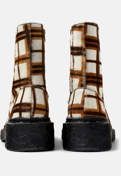 Faux fur ankboots med ett beige och brunt rutig mönster samt en texturerad svart plattformssula. Släta, rundade kanter och dragkedjestängning.